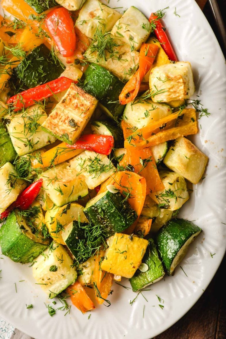 Roasted zucchini and peppers topped with fresh herbs, on a white serving platter.