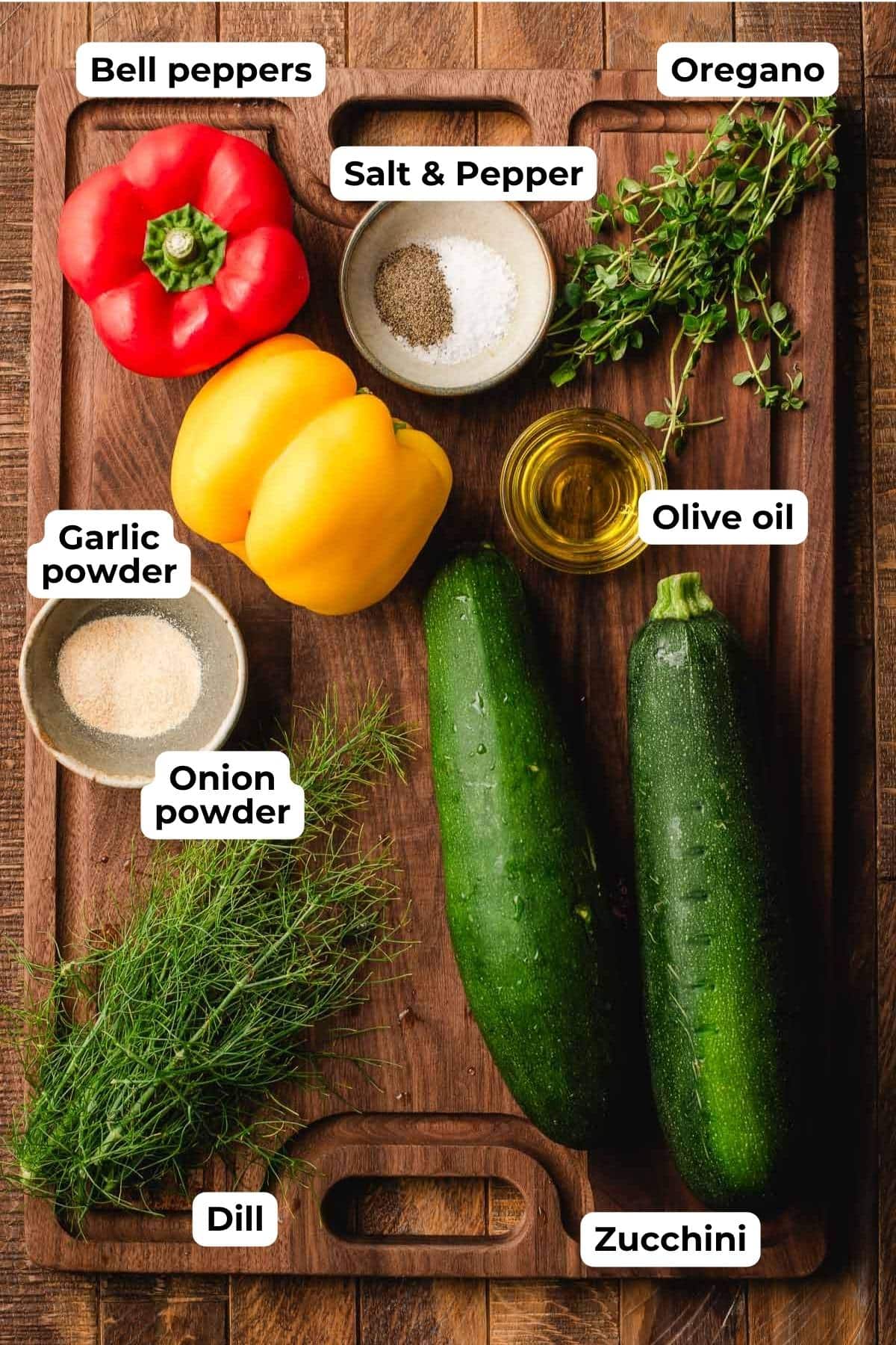 Zucchinis, bell peppers, fresh dill, fresh oregano, olive oil, and seasonings on a wooden cutting board.