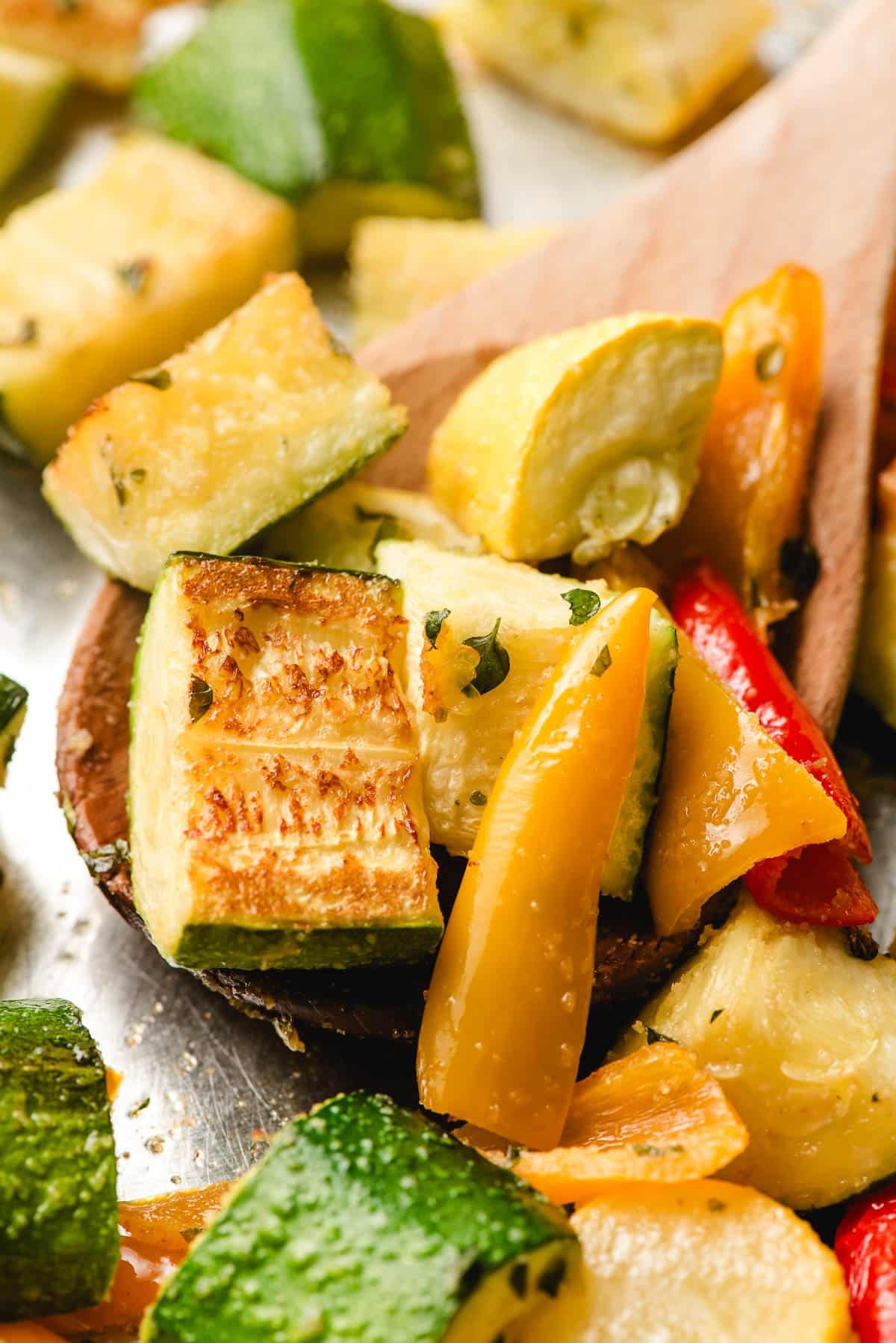 Wooden spoon scooping up roasted zucchini and peppers.
