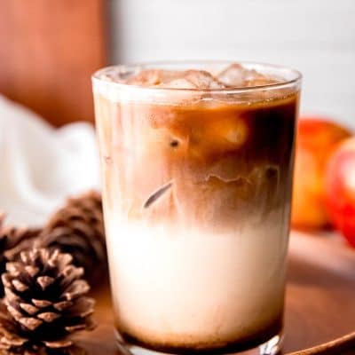Iced Apple Crisp Macchiato in a glass surrounded by pine cones.