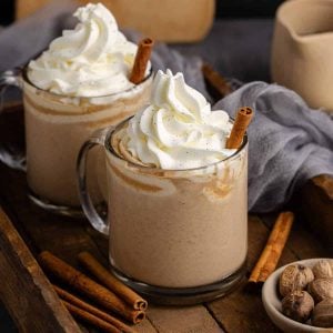 Pumpkin Chai Lattes in glass mugs, topped with a swirl of whipped cream, and a cinnamon stick.