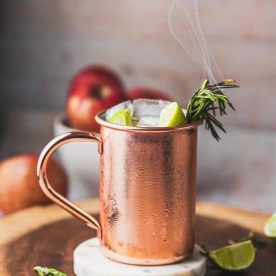 Apple cider moscow mules in a copper mug with lime wedges and rosemary.