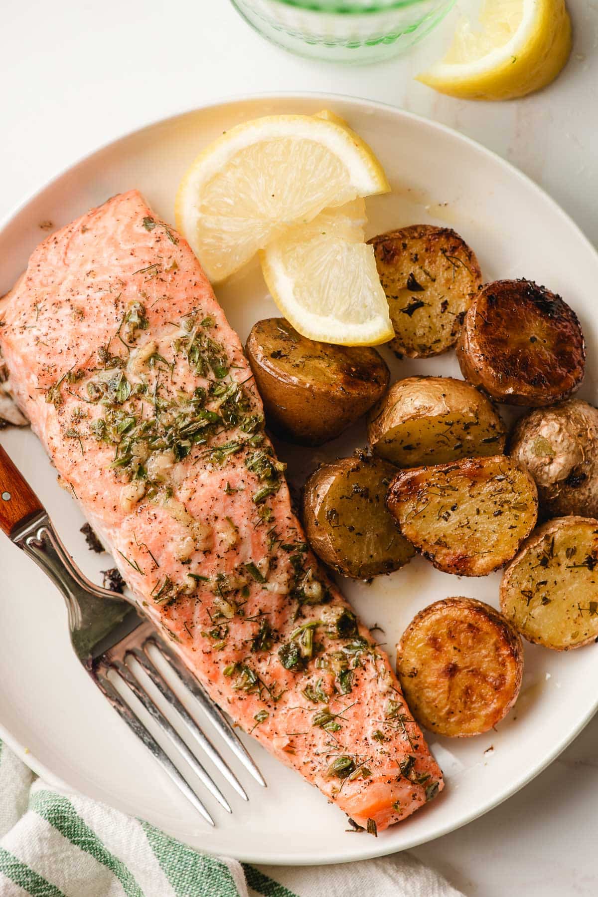 Garlic herb salmon and potatoes on a white plate, with lemon slices.