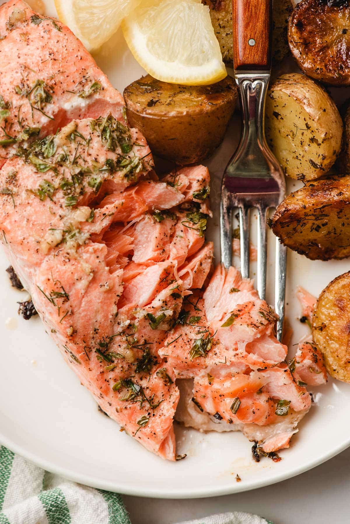 Fork flaking apart herby garlic lemon salmon on a plate.