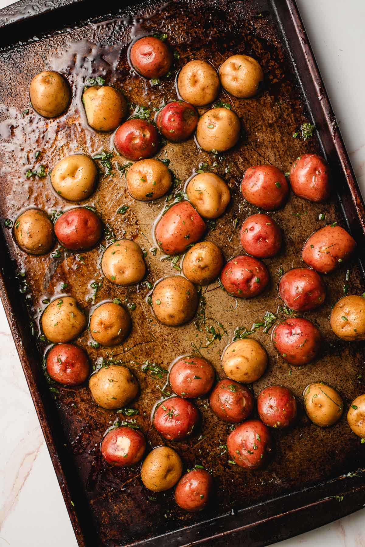 Baby potatoes tossed with garlic herb oil on a baking sheet.