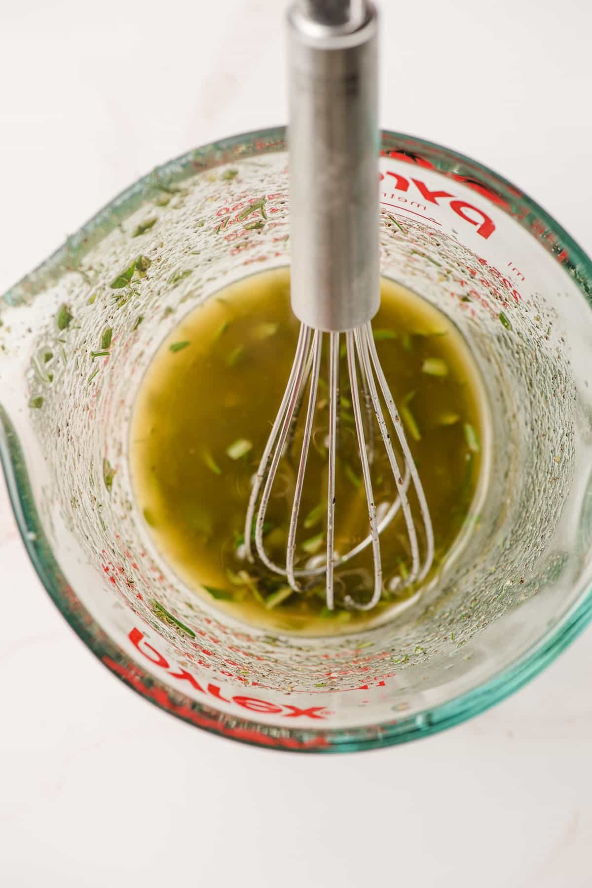 Garlic, lemon juice, olive oil, and fresh herbs in a measuring cup.