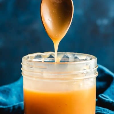 Spoon drizzling maple caramel into a mason jar.