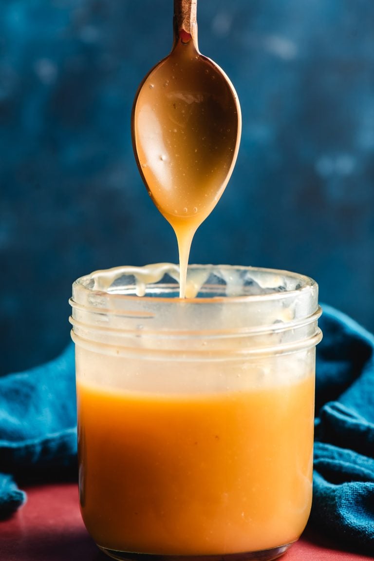 Spoon drizzling maple caramel into a mason jar.
