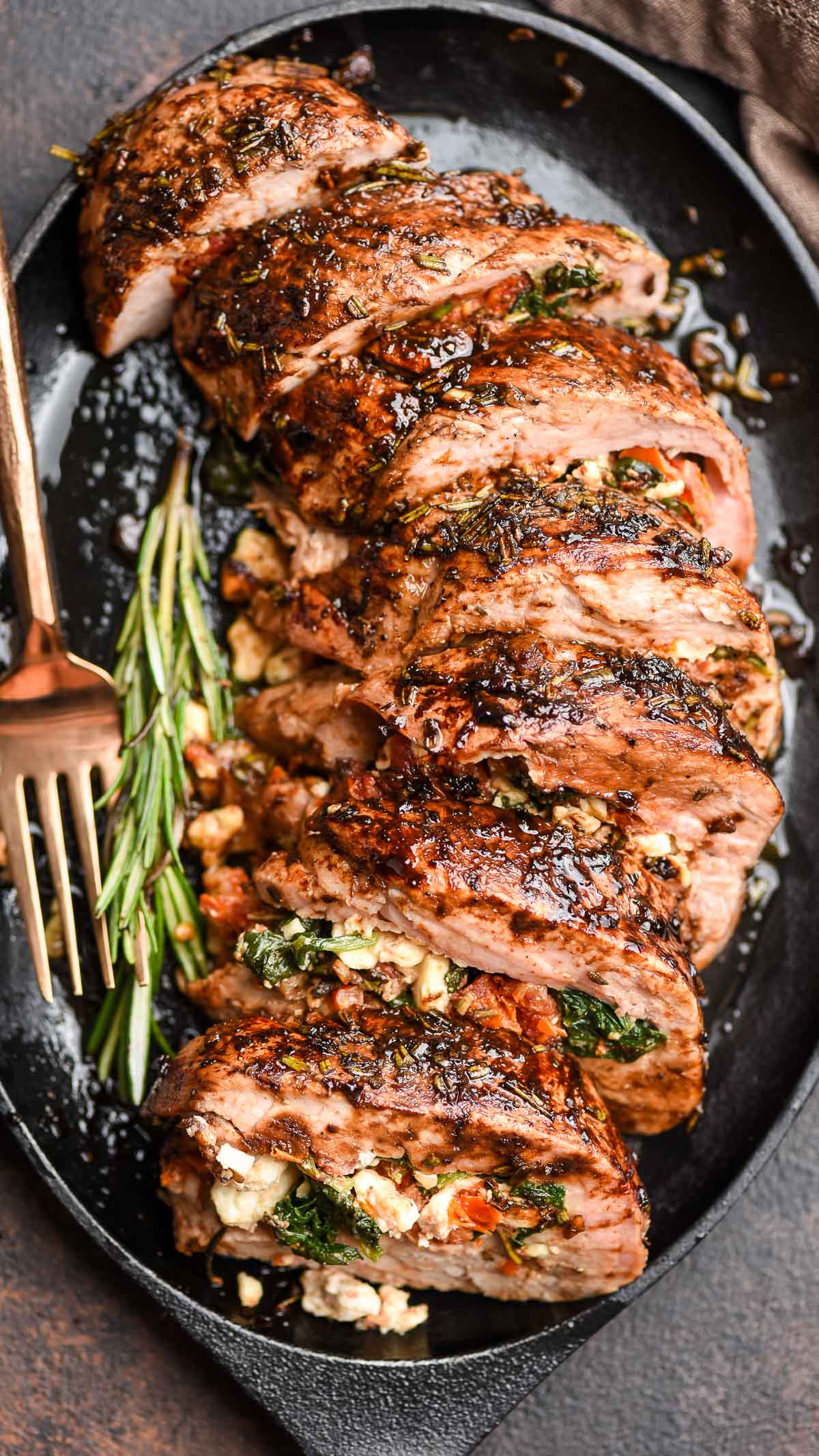stuffed pork tenderloin with spinach, feta, and sundried tomatoes sliced on a serving platter.