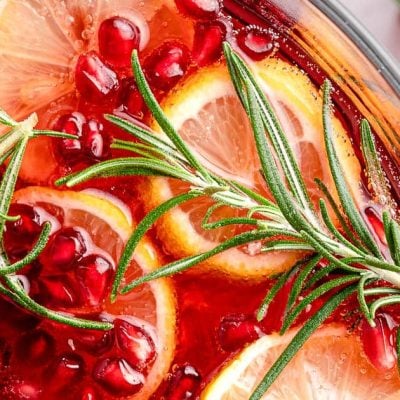 Punch in a glass with pomegranate seeds, orange slices, and fresh sprigs of rosemary.