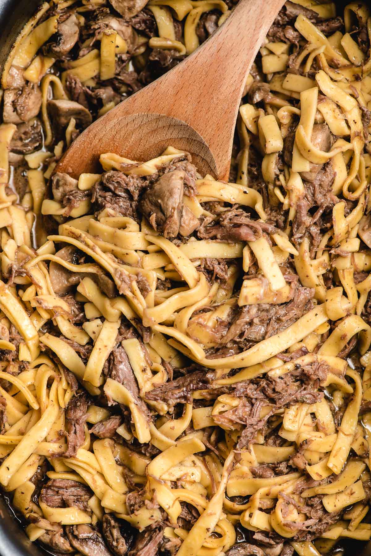 a wooden spoon stirring beef and noodles to combine all of the delicious flavor before serving. 
