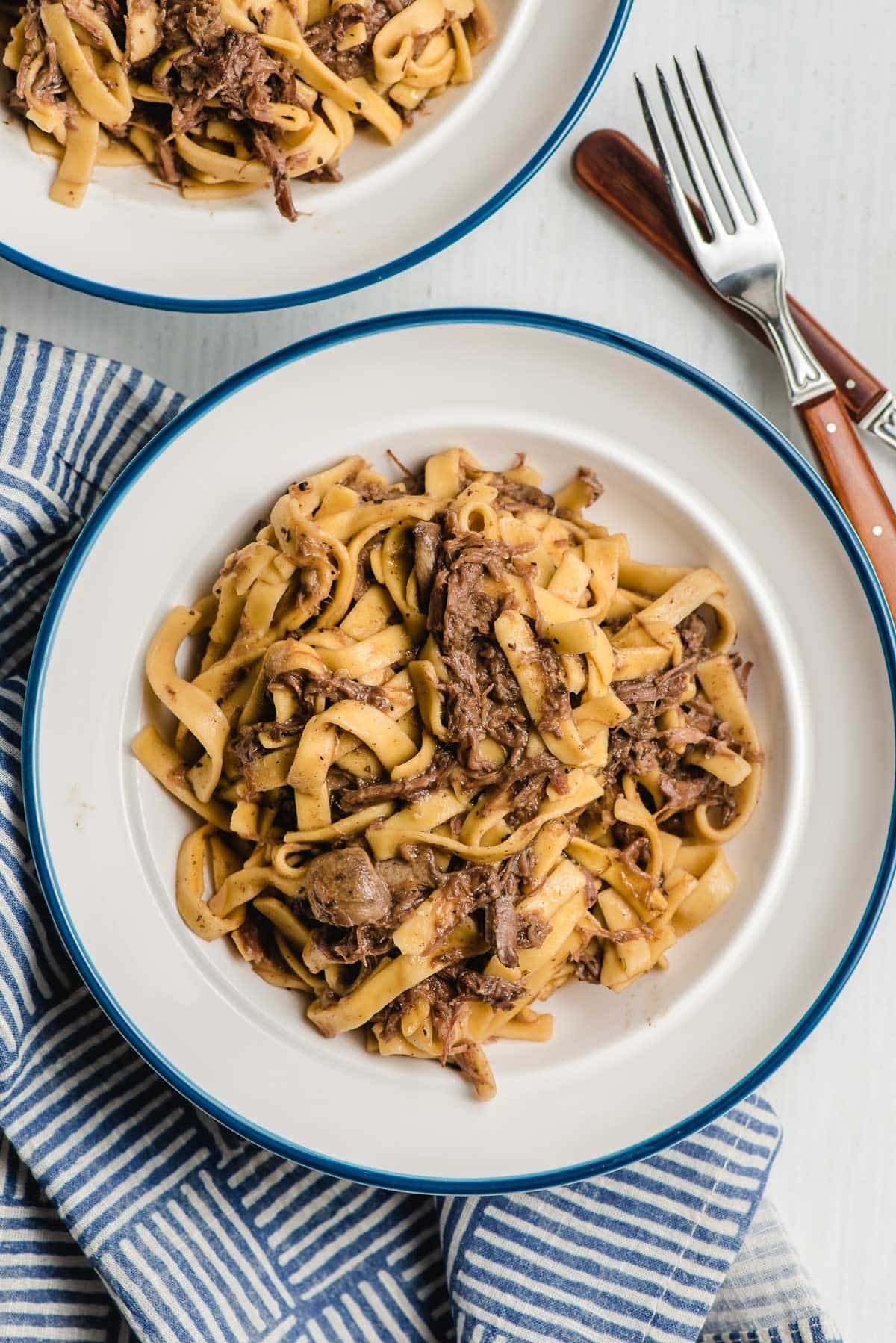 slow cooker beef and noodles in a white bowl with tender pieces of beef shredded to perfection.