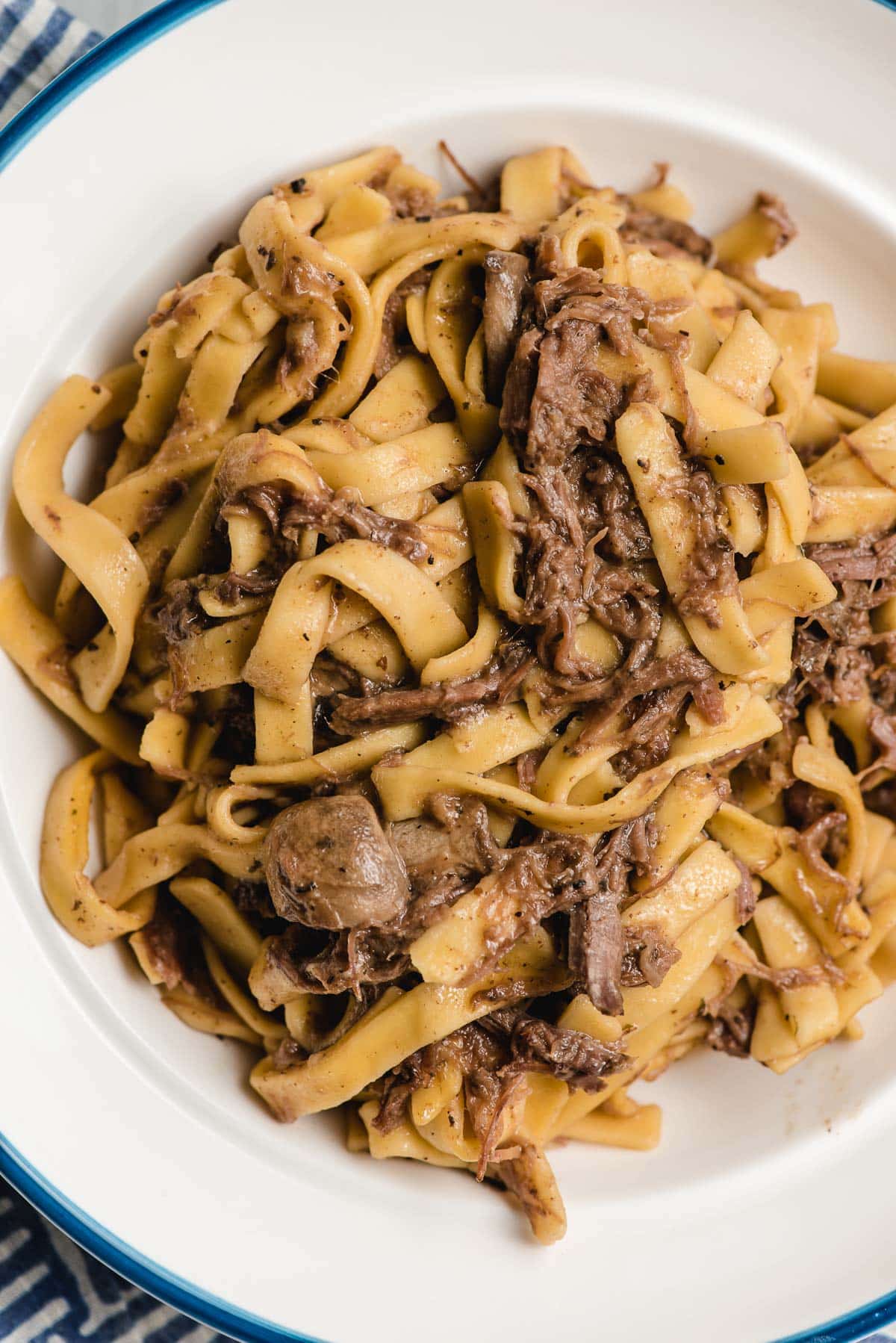 a bowl of slow cooker beef and noodles served in a white bowl. 