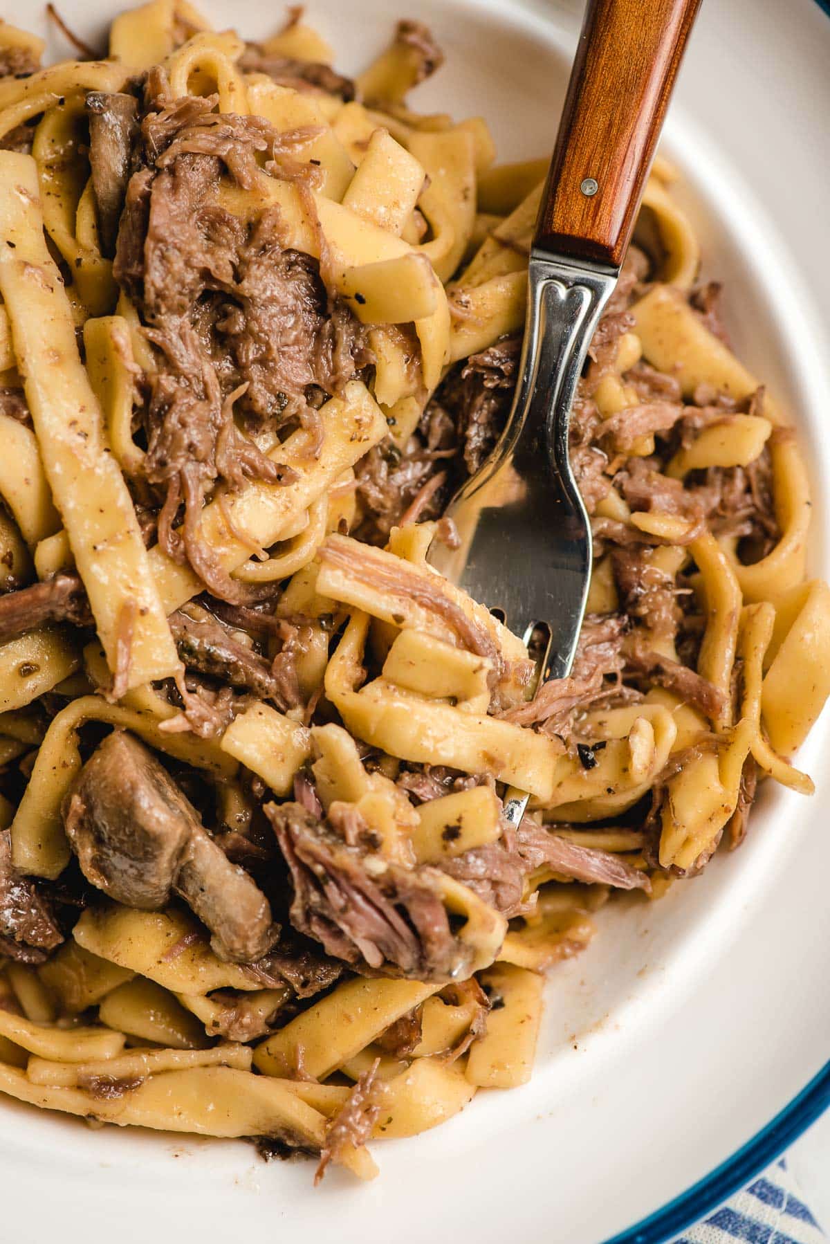 a fork resting with a bite of noodles and beef picked up from the bowl. 