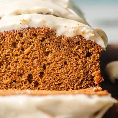 Slice of frosted pumpkin bread on a wooden cutting board.
