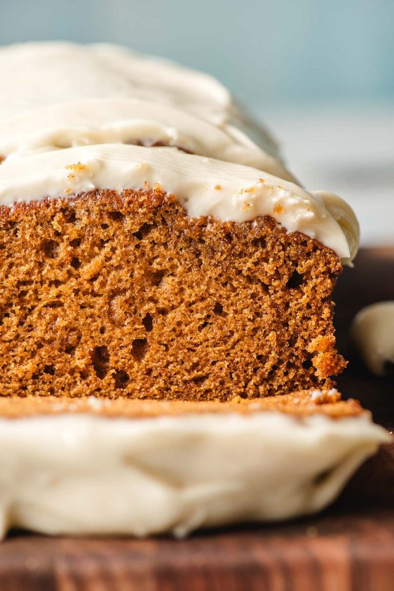 Slice of frosted pumpkin bread on a wooden cutting board.
