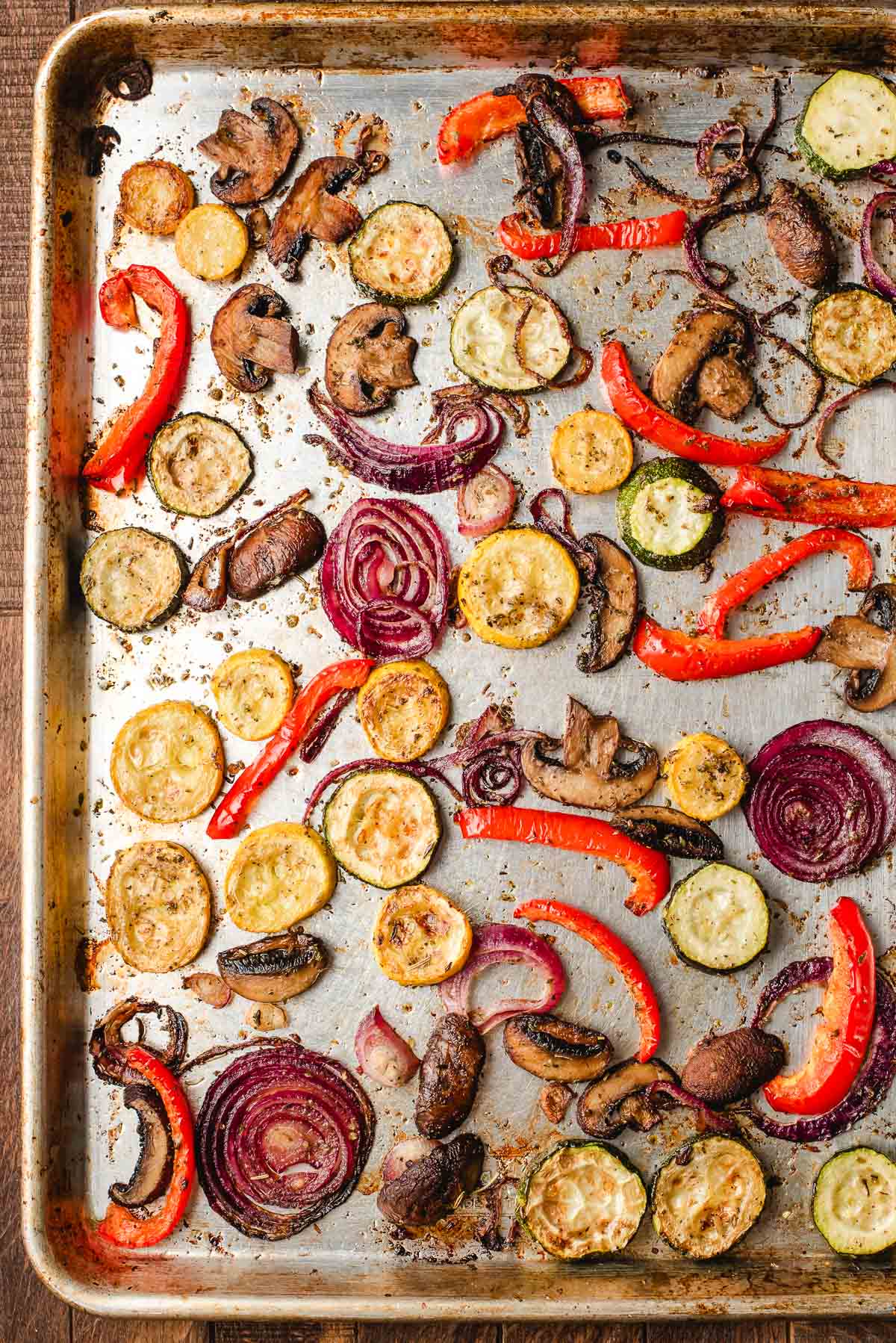 Sheet pan filled with roasted vegetables, including zucchini, squash, mushrooms, red pepper, and red onion.