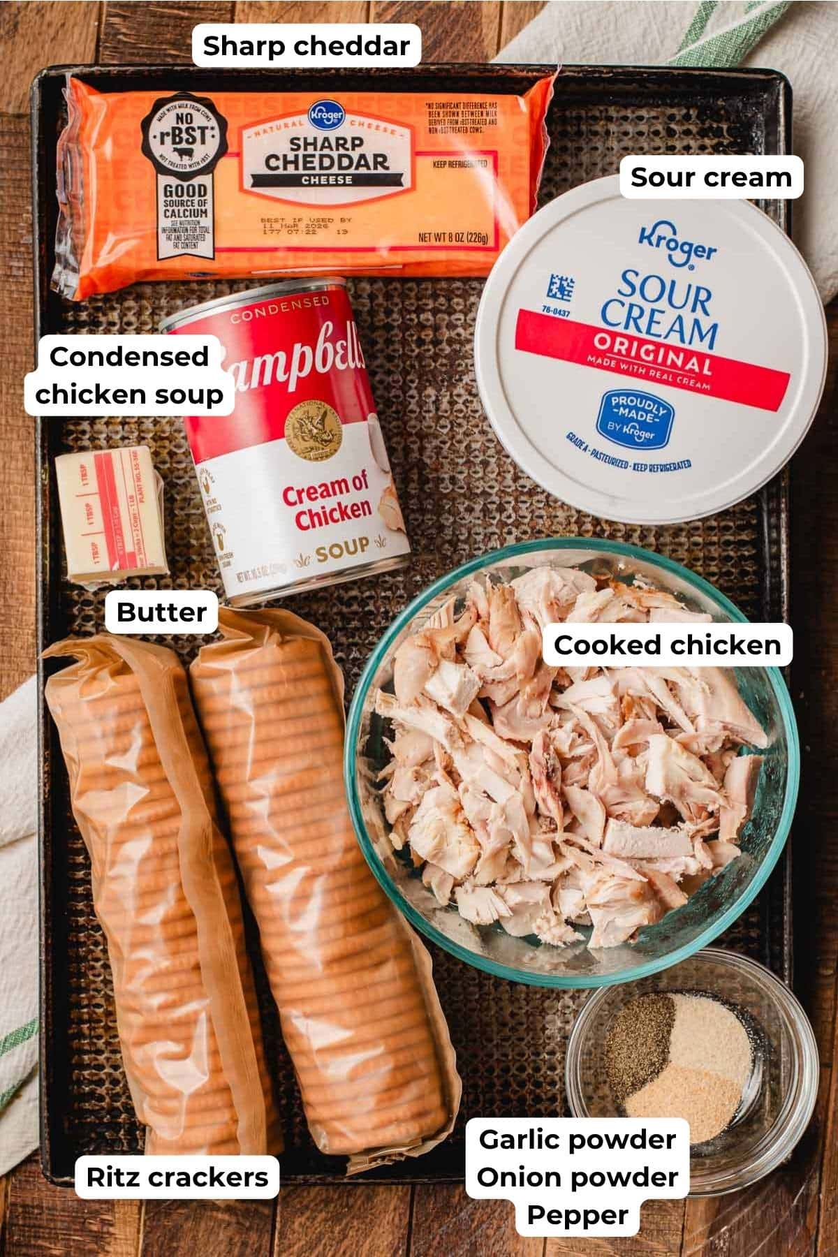 Block of cheddar cheese, sour cream, canned soup, butter, sleeves of ritz crackers, cooked chicken, and seasonings on a sheet pan.