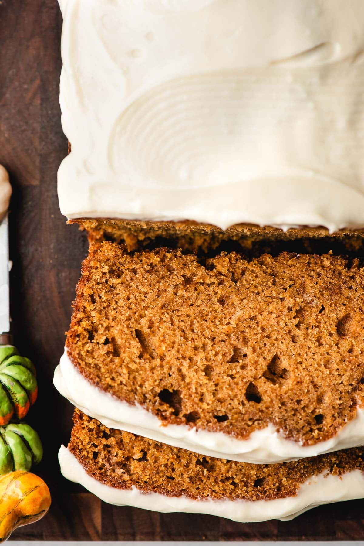 Sliced pumpkin bread with cream cheese frosting on a cutting board.