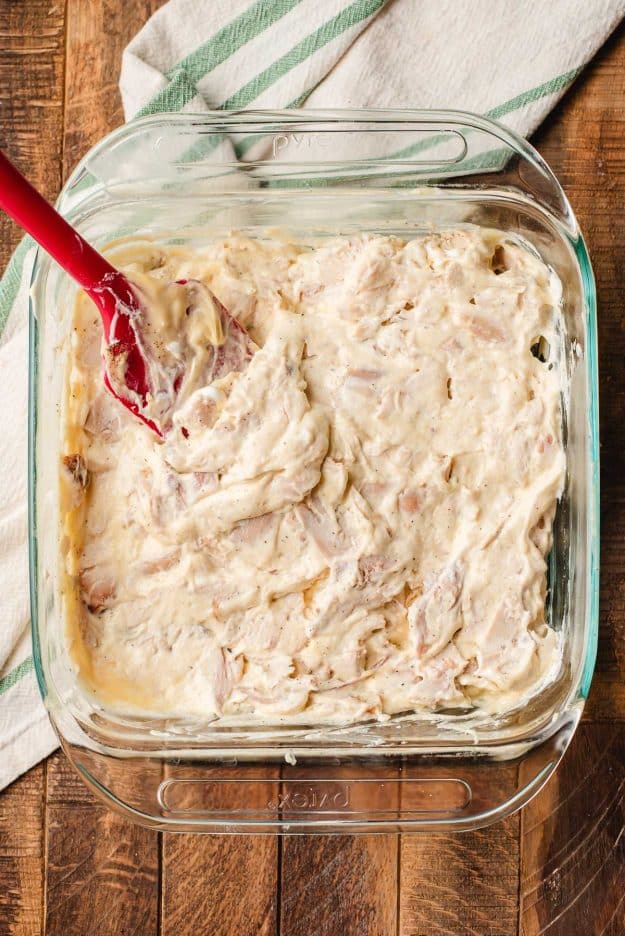 Cooked chicken stirred together with canned soup, sour cream, and spices in a glass casserole dish.