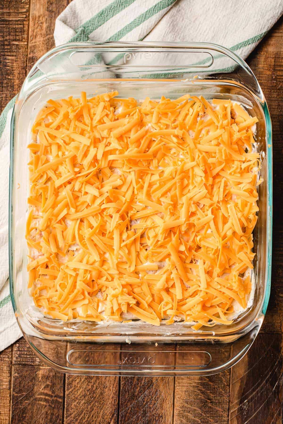 Shredded cheese covering a layer of creamy chicken in a casserole dish.