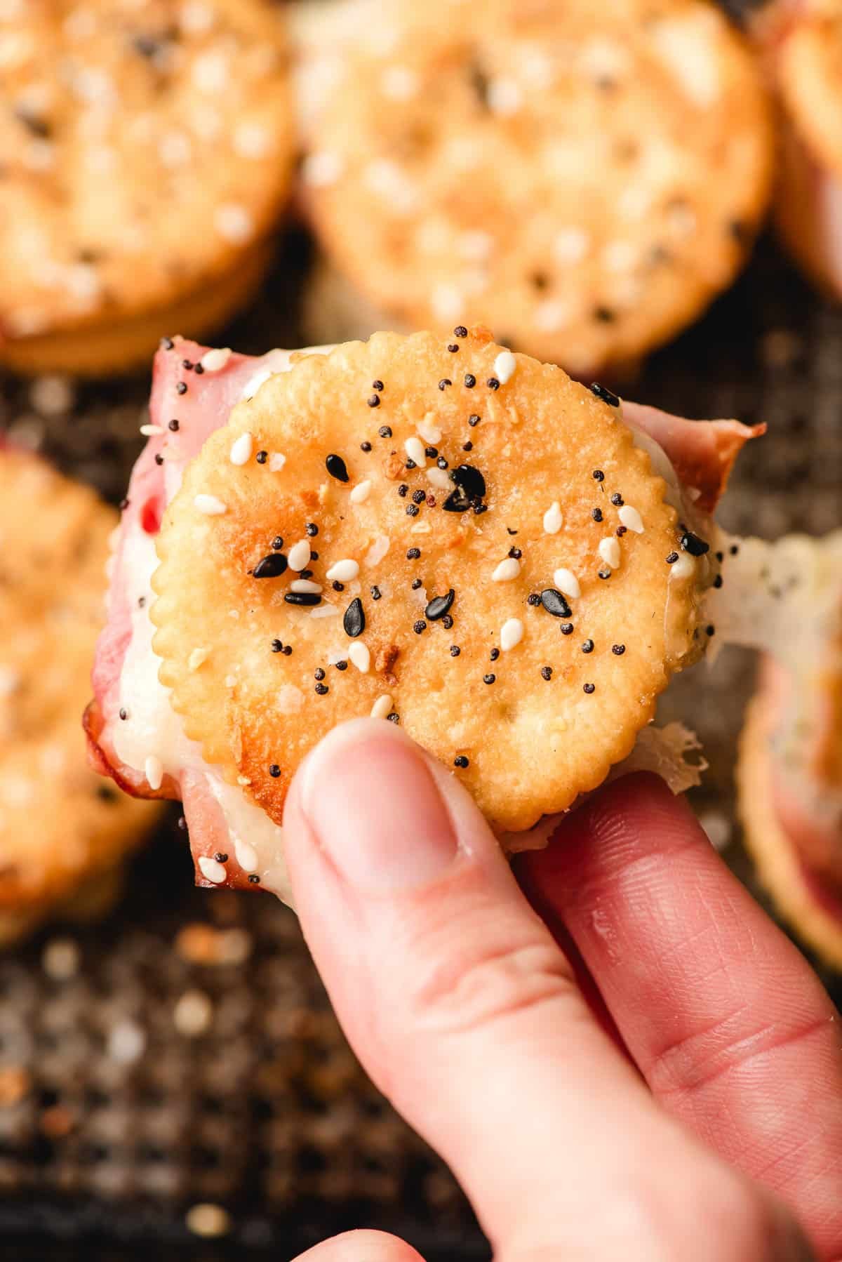 Hand holding a ham and cheese cracker sandwich.