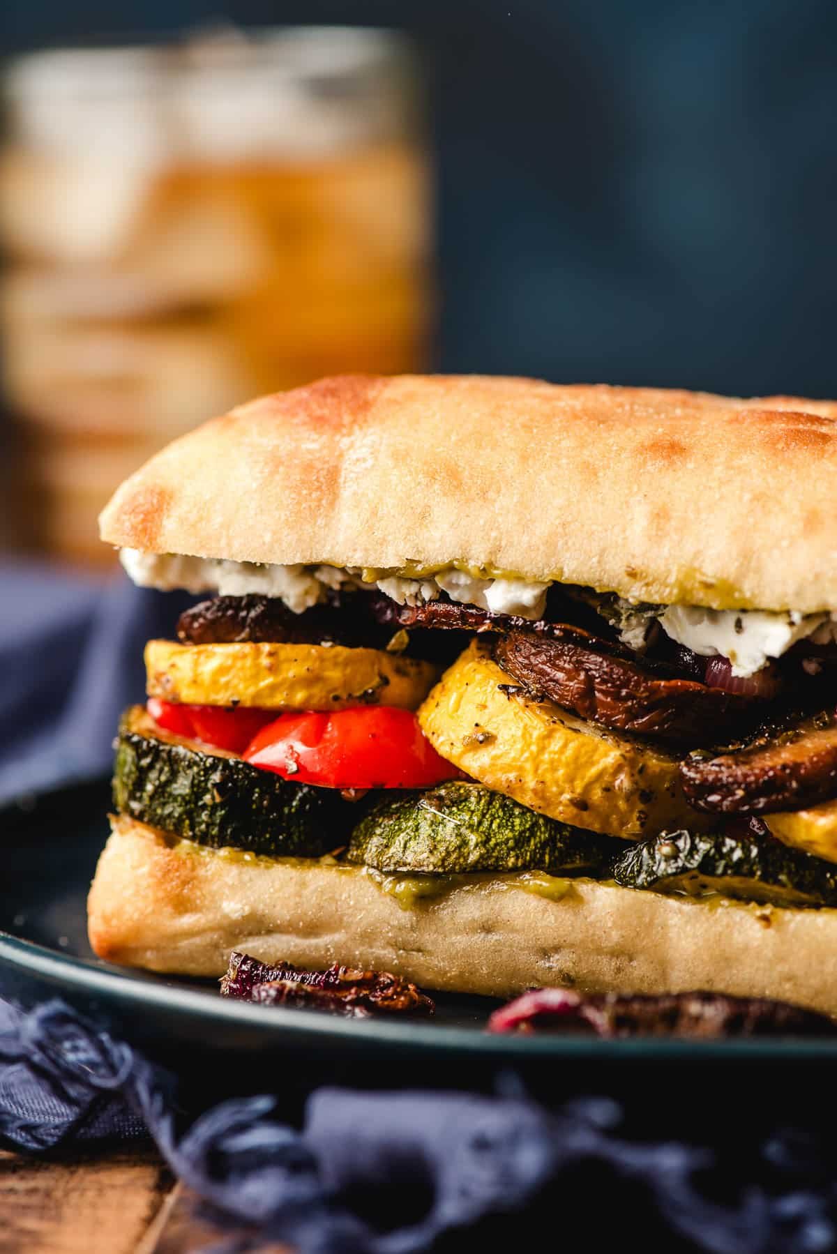 Roasted veggie sandwich with pesto and goat cheese on a blue plate.