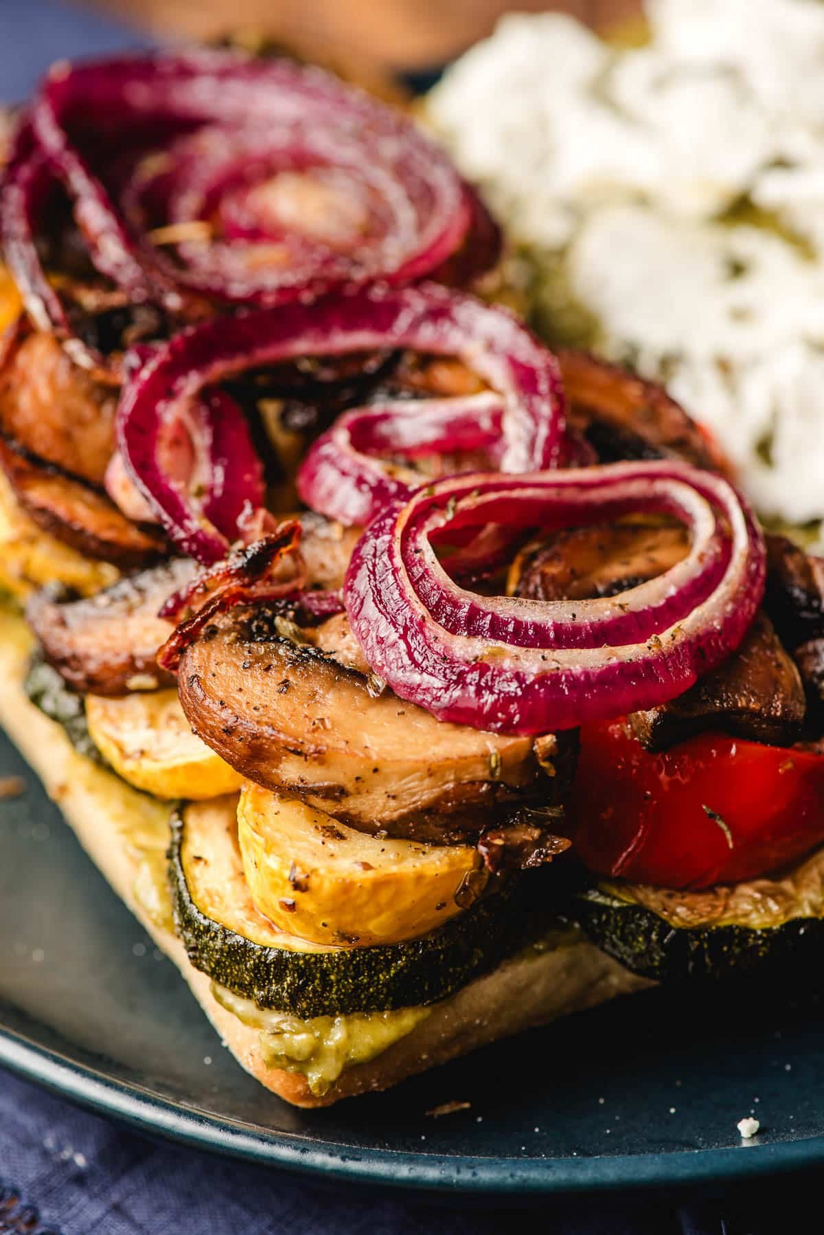 Open face vegetable sandwich stacked with roasted zucchini, squash, mushrooms, and red onion.