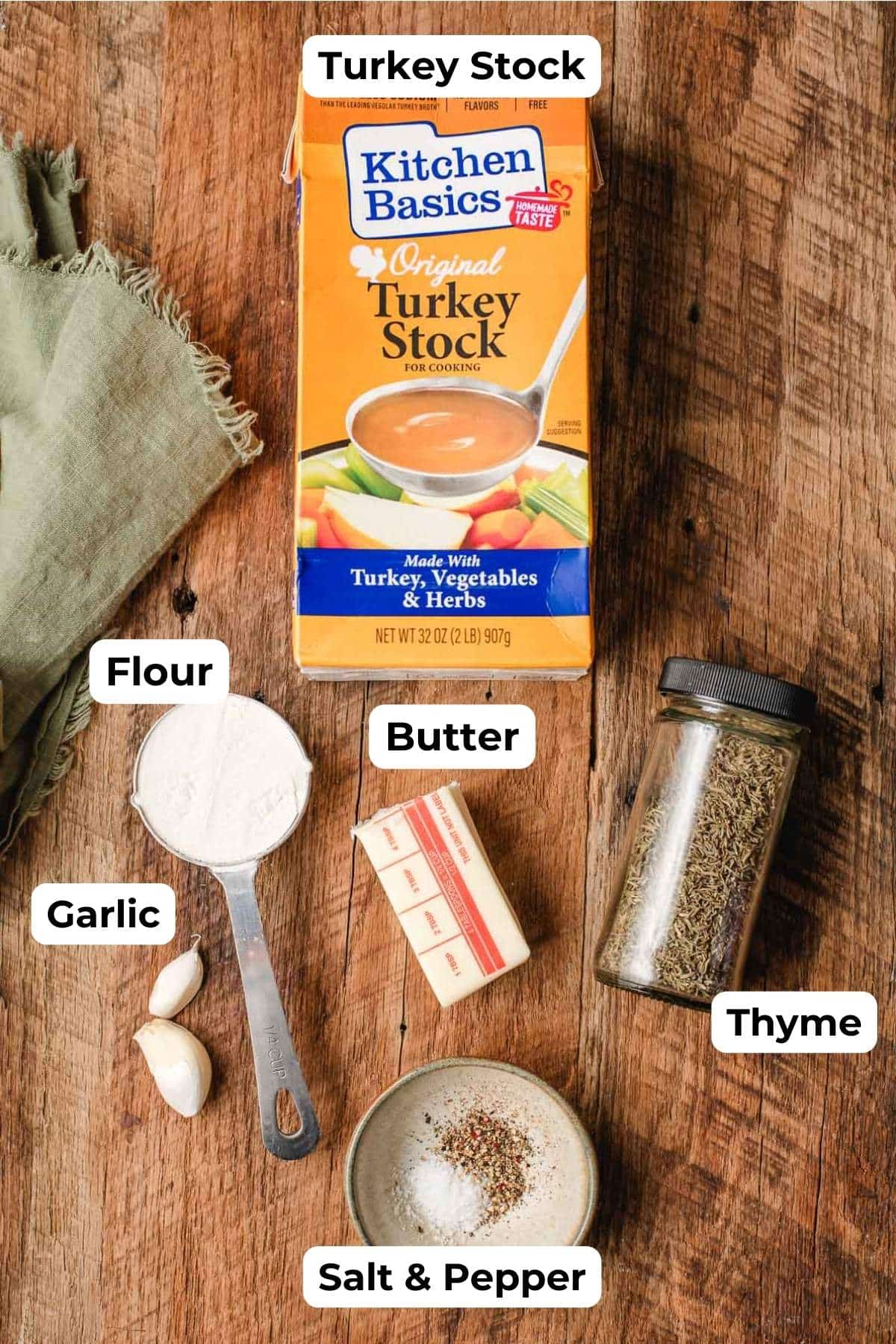 Turkey stock, flour, garlic cloves, butter, thyme, and salt and pepper on a wood background.