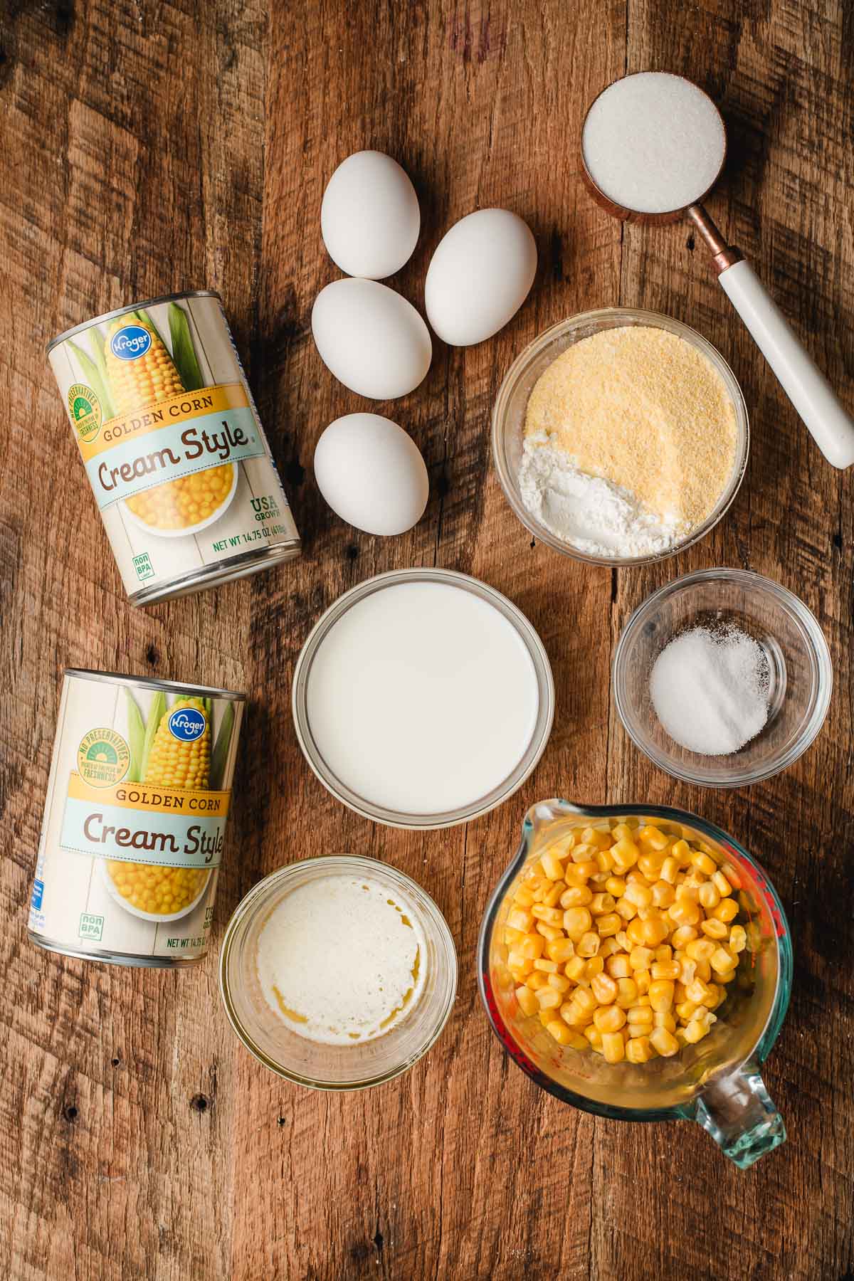 recipe ingredients for corn souffle including corn, eggs, and spices on a wooden surface