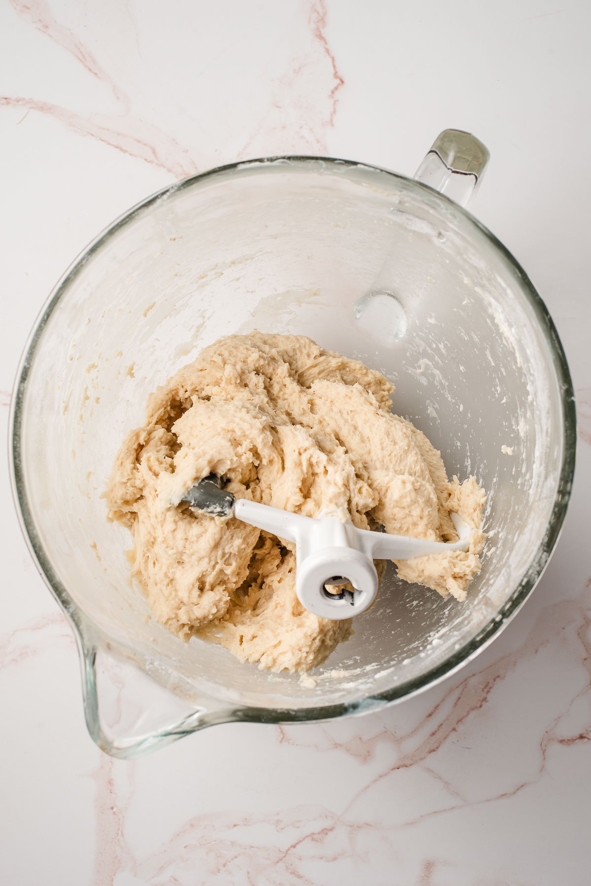 dinner roll dough in a glass mixing bowl with beater