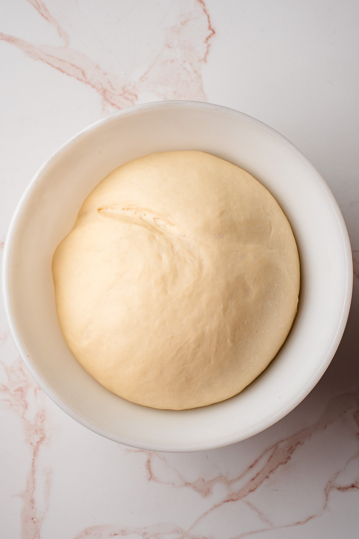 Risen dinner roll dough in a white bowl.