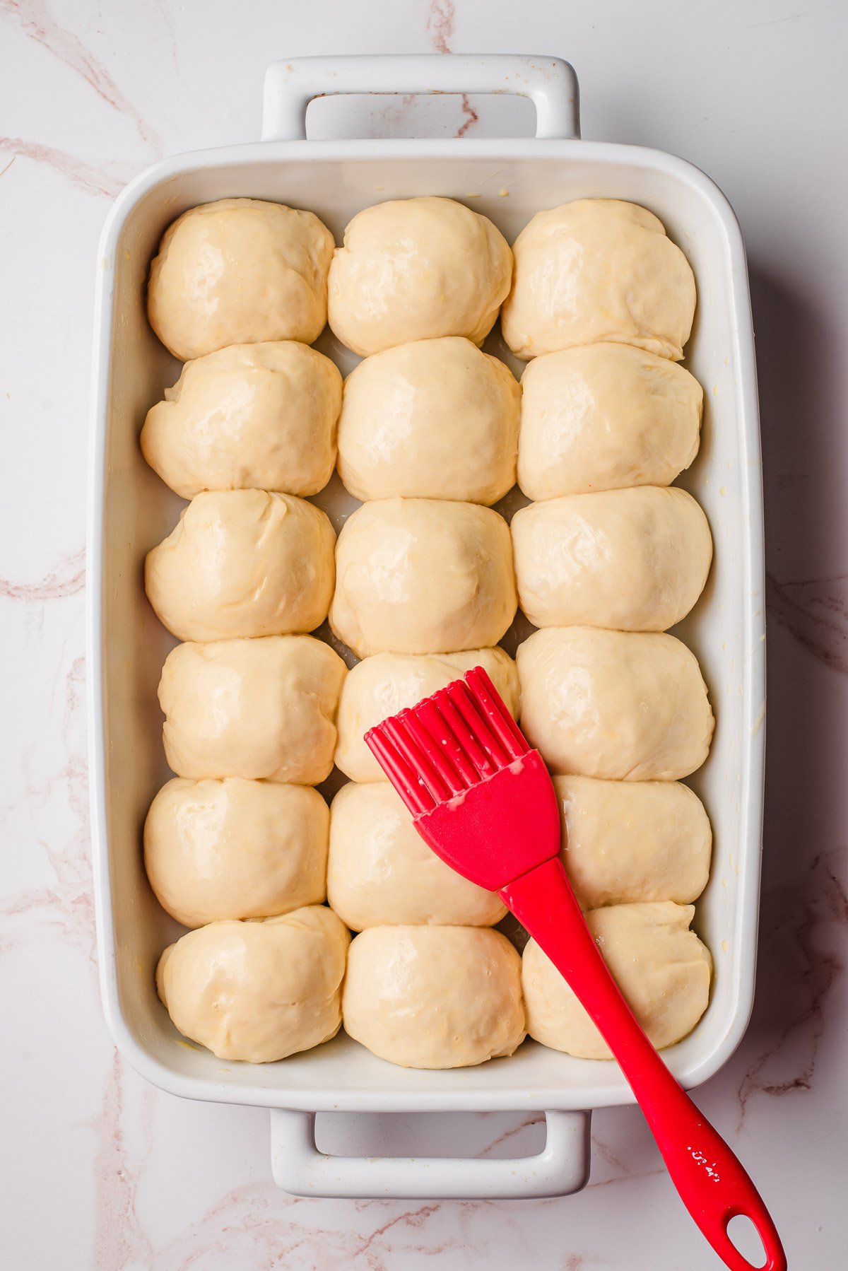 Unbaked yeast rolls brushed with egg wash in a casserole dish.