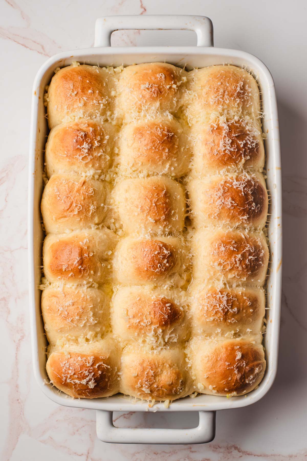 Freshly baked garlic dinner rolls in a casserole dish, sprinkled with grated Parmesan cheese.