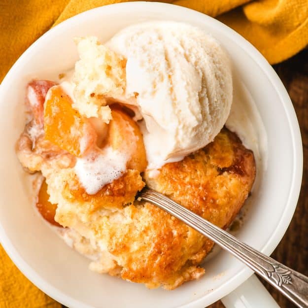 Biscuit peach cobbler in a bowl topped with a scoop of ice cream.