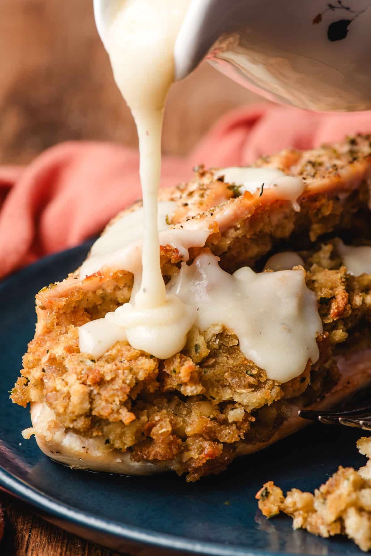 pouring gravy over stuffing stuffed chicken on a blue plate. 