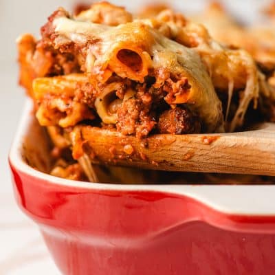 Wooden spoon scooping up a portion of baked rigatoni.