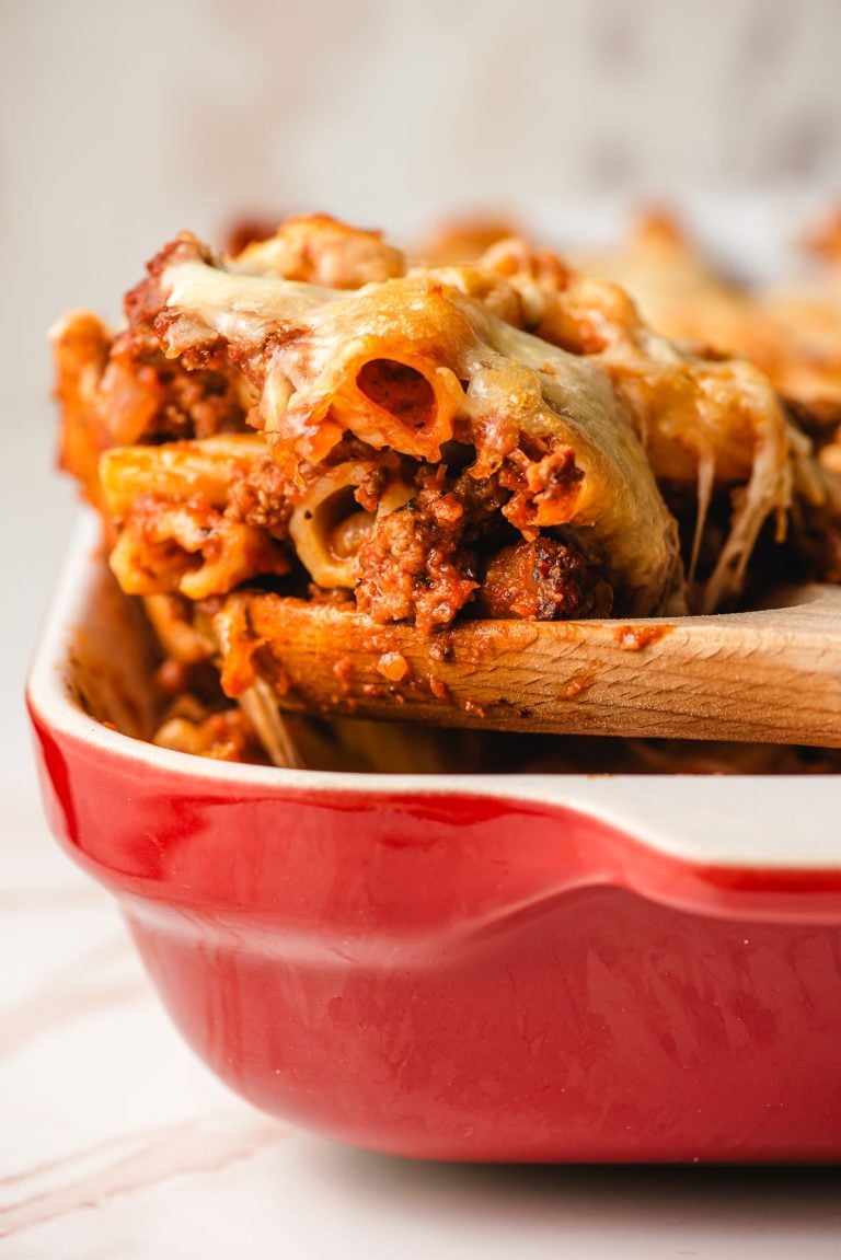 Wooden spoon scooping up a portion of baked rigatoni.