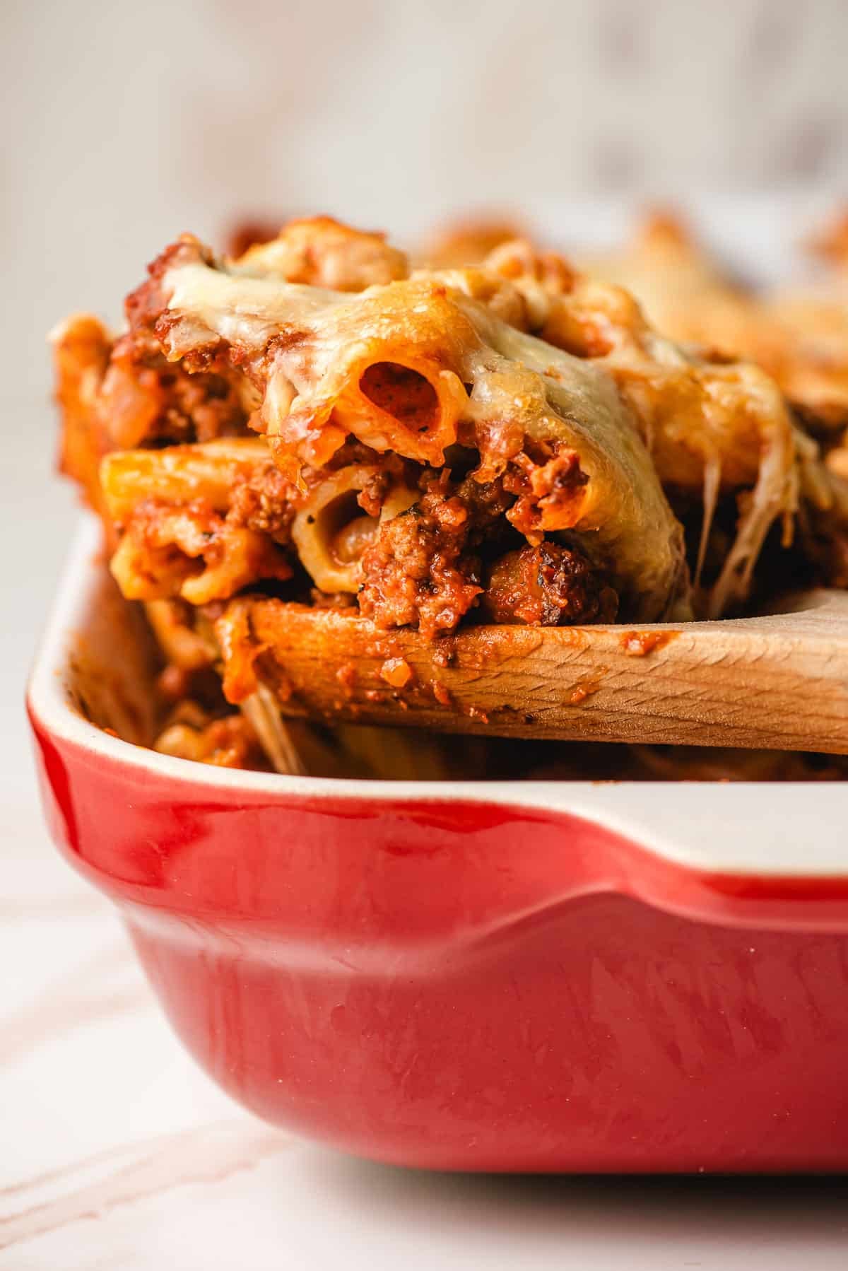 Wooden spoon scooping up a portion of baked rigatoni.