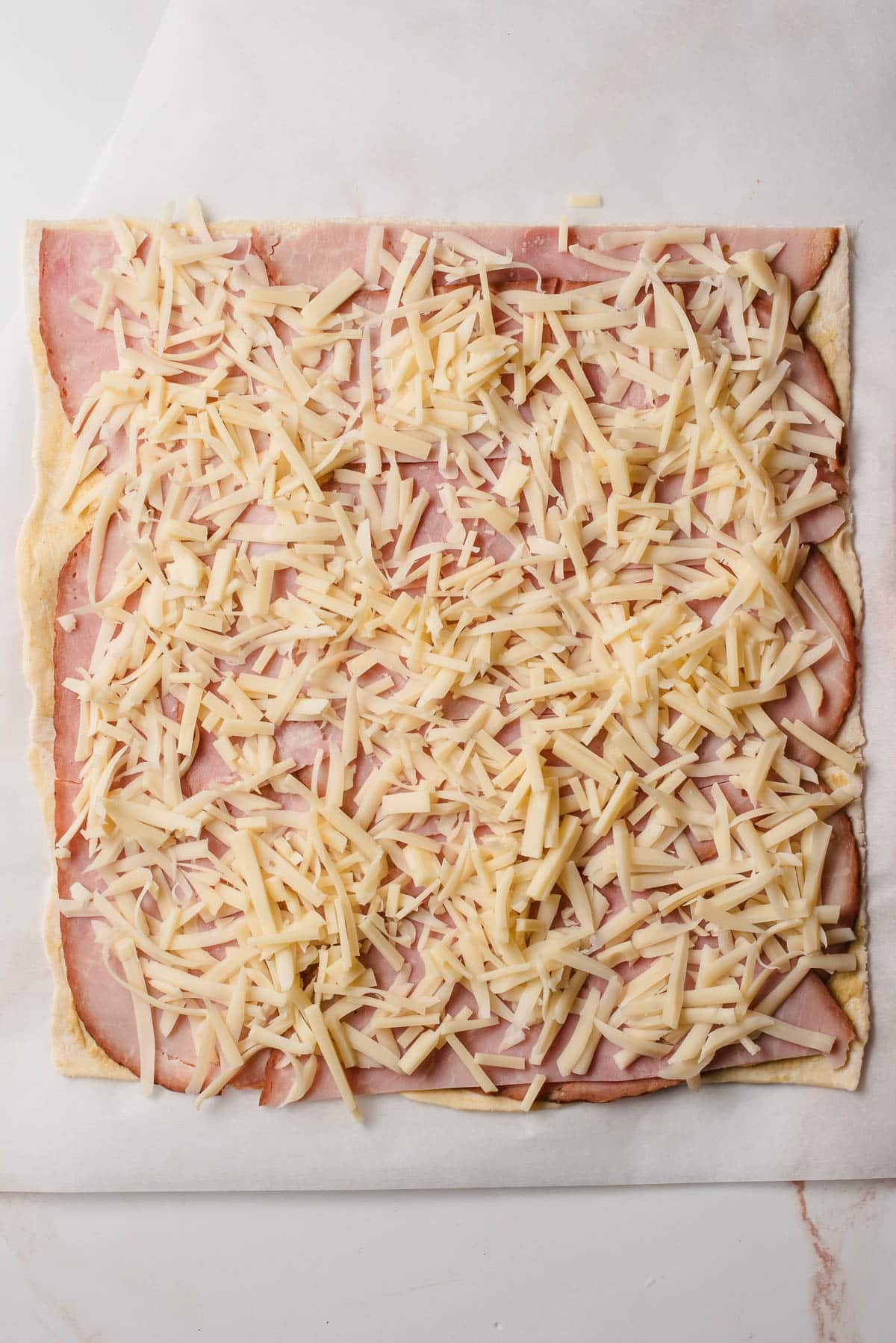 Shredded Swiss cheese on top of ham and puff pastry.