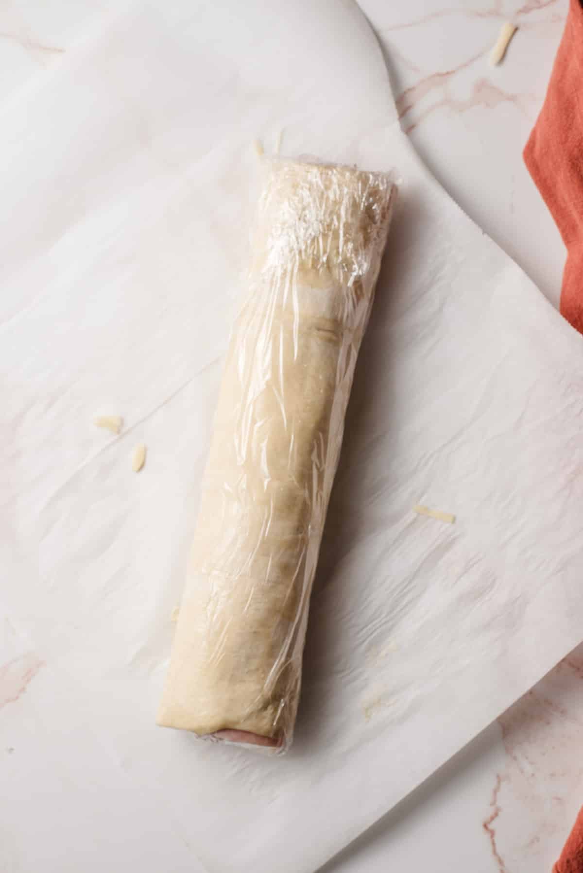 Rolled ham and cheese puff pastry wrapped in saran wrap.