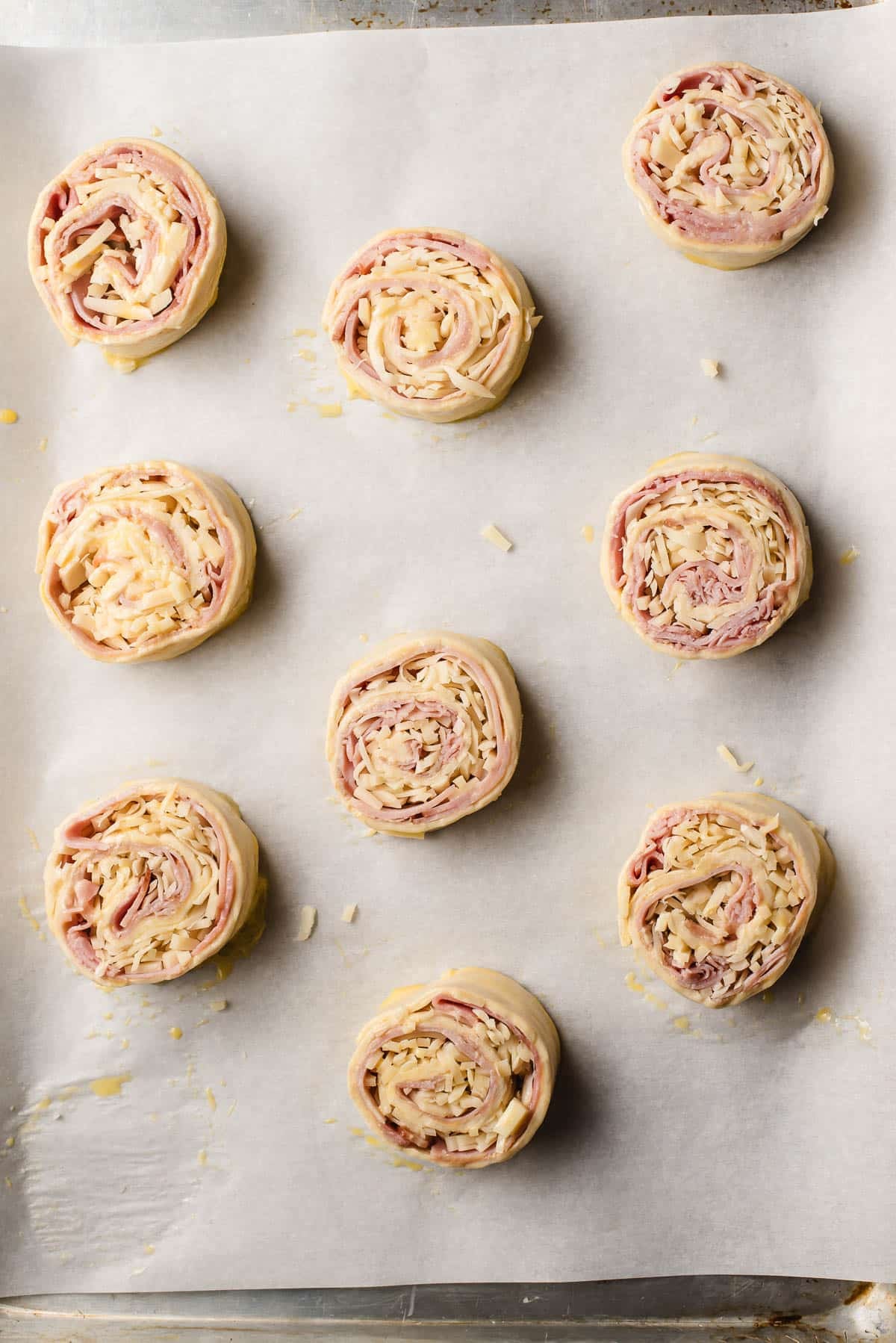 Unbaked ham and cheese puff pastry rolls on a baking sheet.