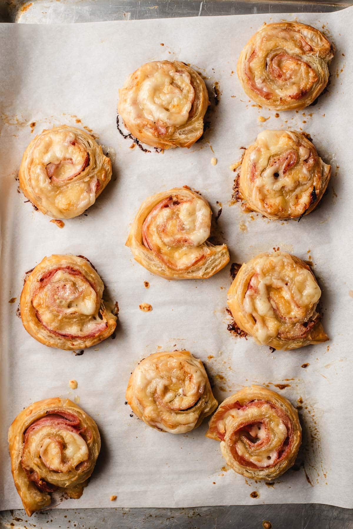 Freshly baked ham and cheese pinwheels on a baking sheet.