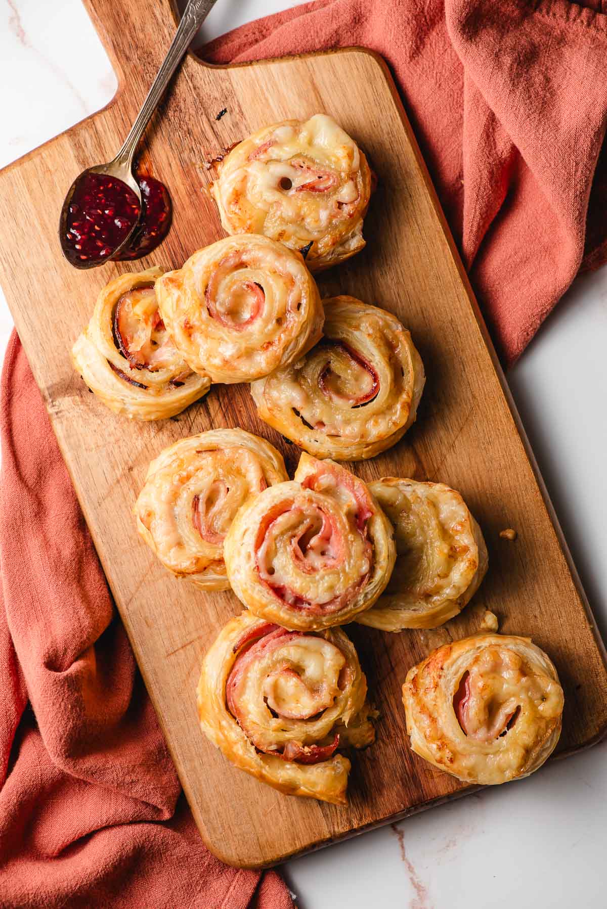 Ham and cheese puff pastries piled on a wooden cutting board.