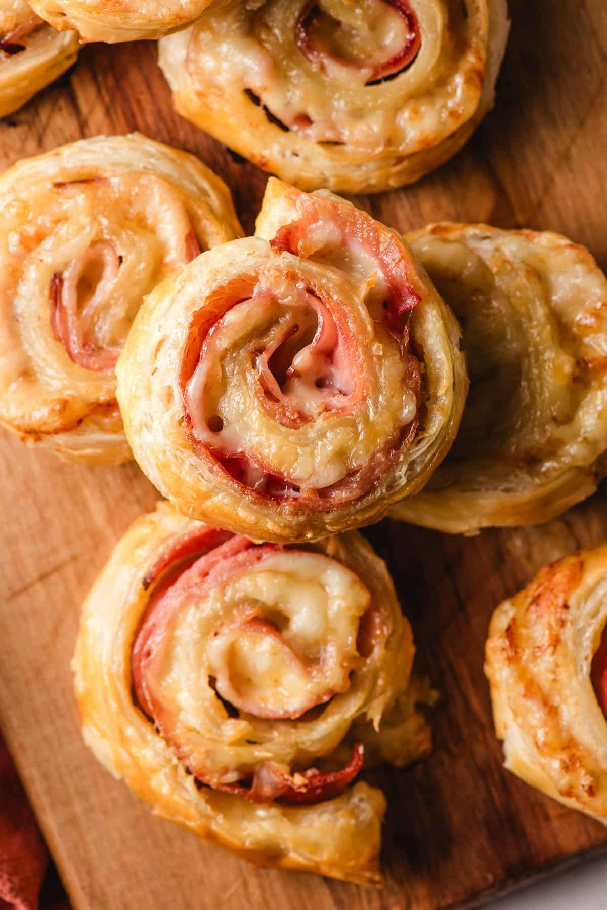 Ham and cheese puff pastry bites on a wooden cutting board.