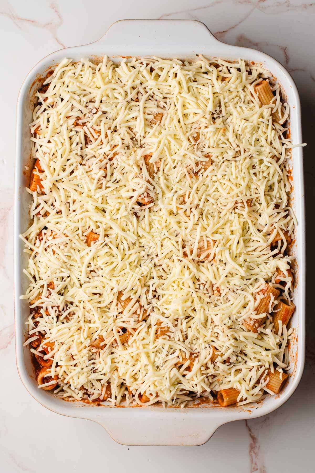 Cheese topped rigatoni in a casserole dish.