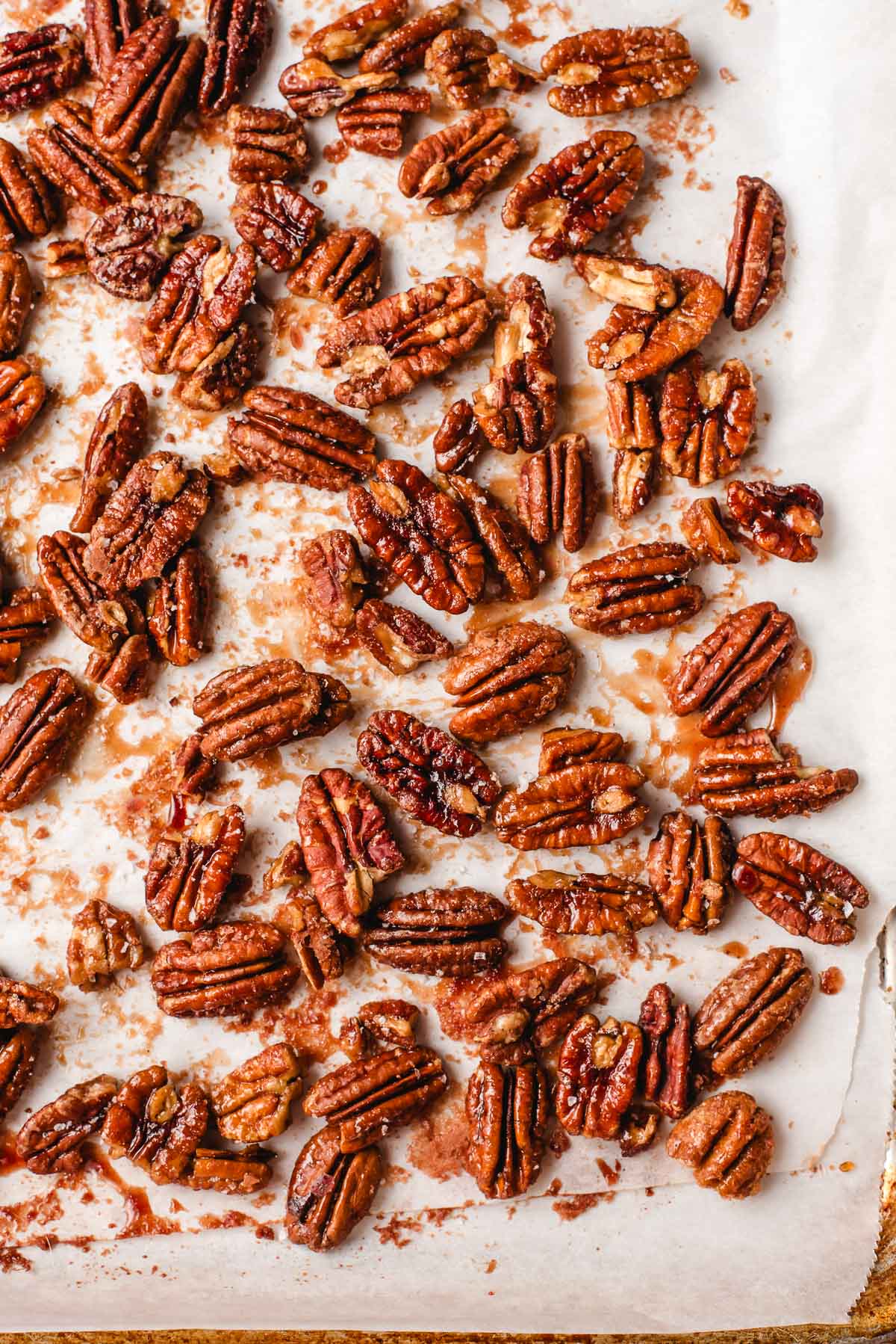 Roasted maple pecans on a parchment lined baking sheet.