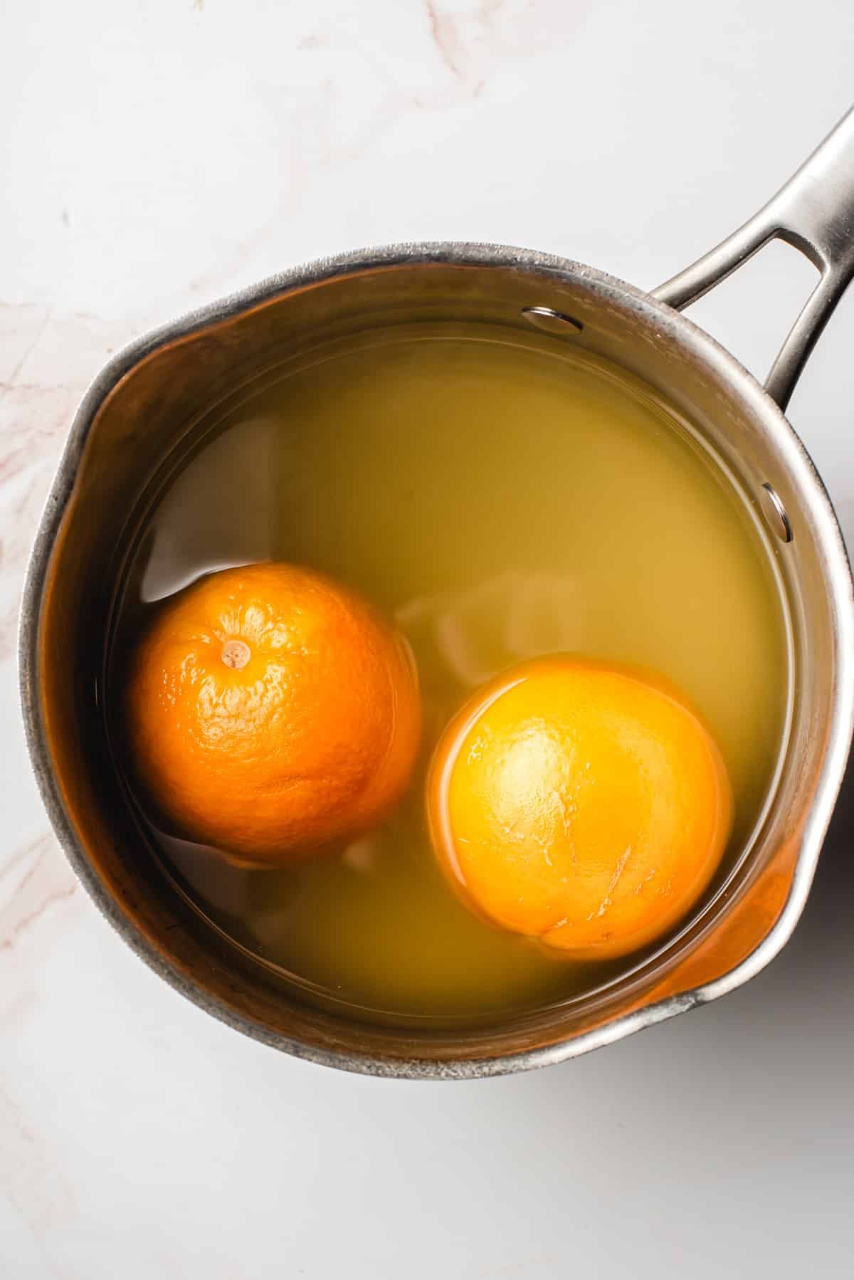 whole oranges boiling in a saucepan