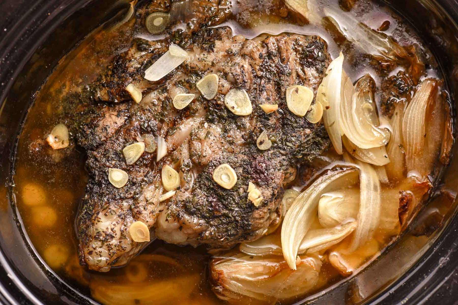 Shredded beef in a slow cooker with sliced onions and garlic.