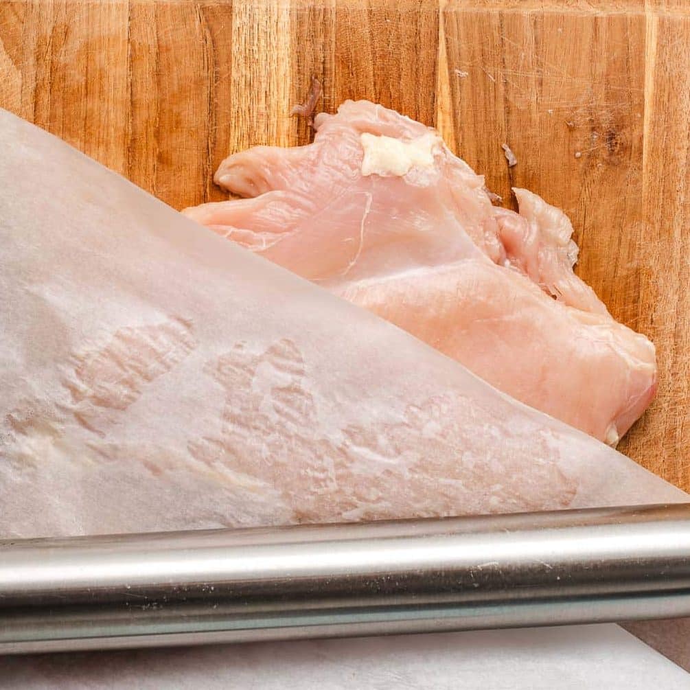 Chicken breast on a cutting board with a rolling pin.